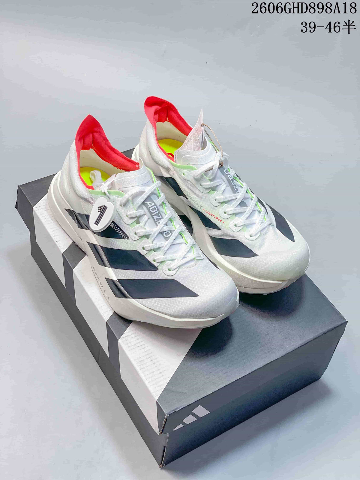 Pair of white Adidas Adizero running shoes with dark side stripes, red heel lining, and lime accents, displayed on a shoebox.
