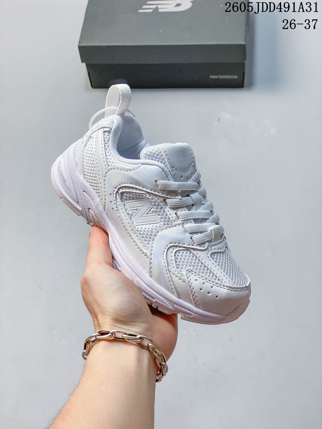 White kids' New Balance 530 lace-up sneaker shown in hand.