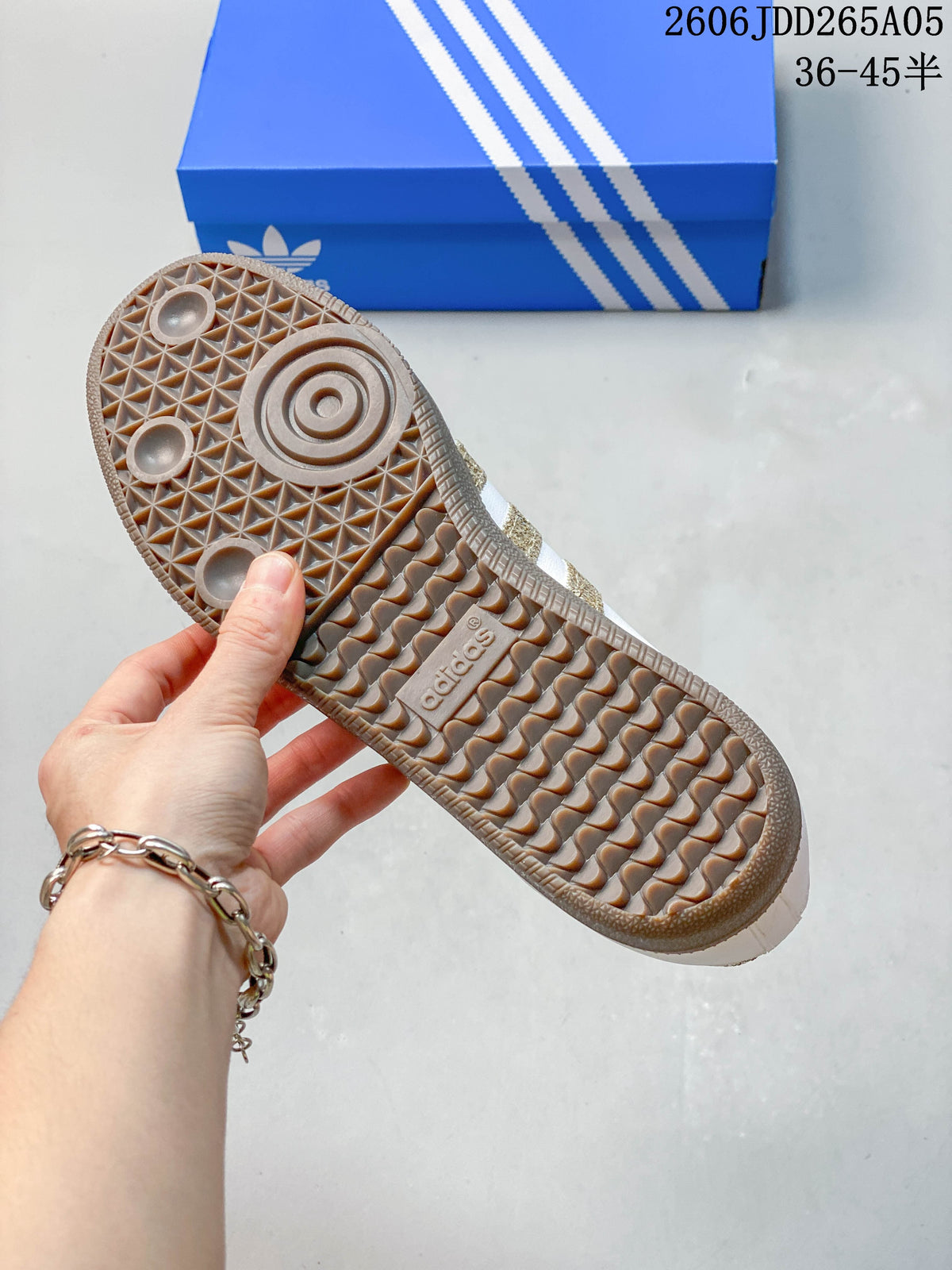 Close-up of the gum-colored outsole and patterned tread on a white and gold Samba OG sneaker.
