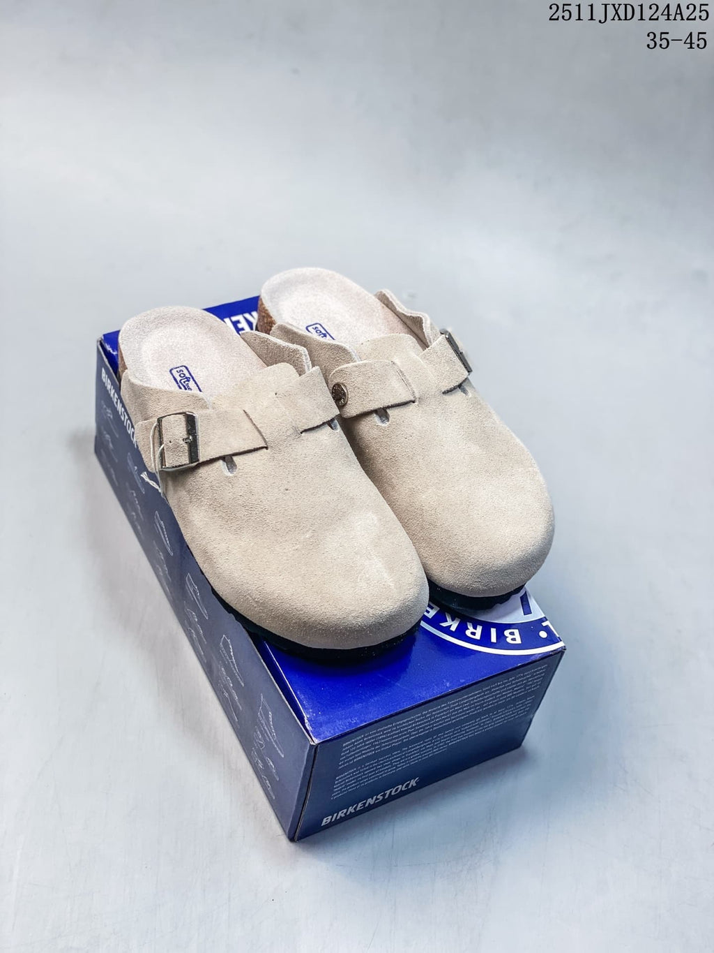 Pair of taupe closed-toe clogs with buckle straps displayed on a blue shoe box