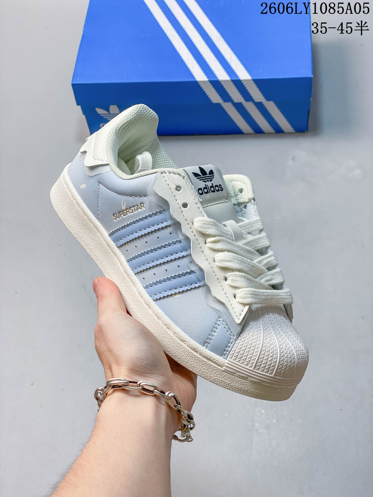 Side view of a pale blue Superstar sneaker with cream details and white laces