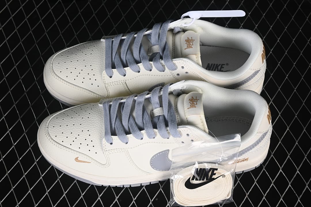 Pair of off-white Nike SB Dunk Low sneakers with grey laces and Swooshes, gold-tone details, and extra laces.