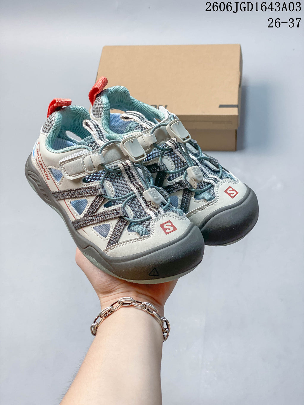 Pair of light gray and blue-gray kids’ Salomon sneakers with cord lacing and a hook-and-loop strap.