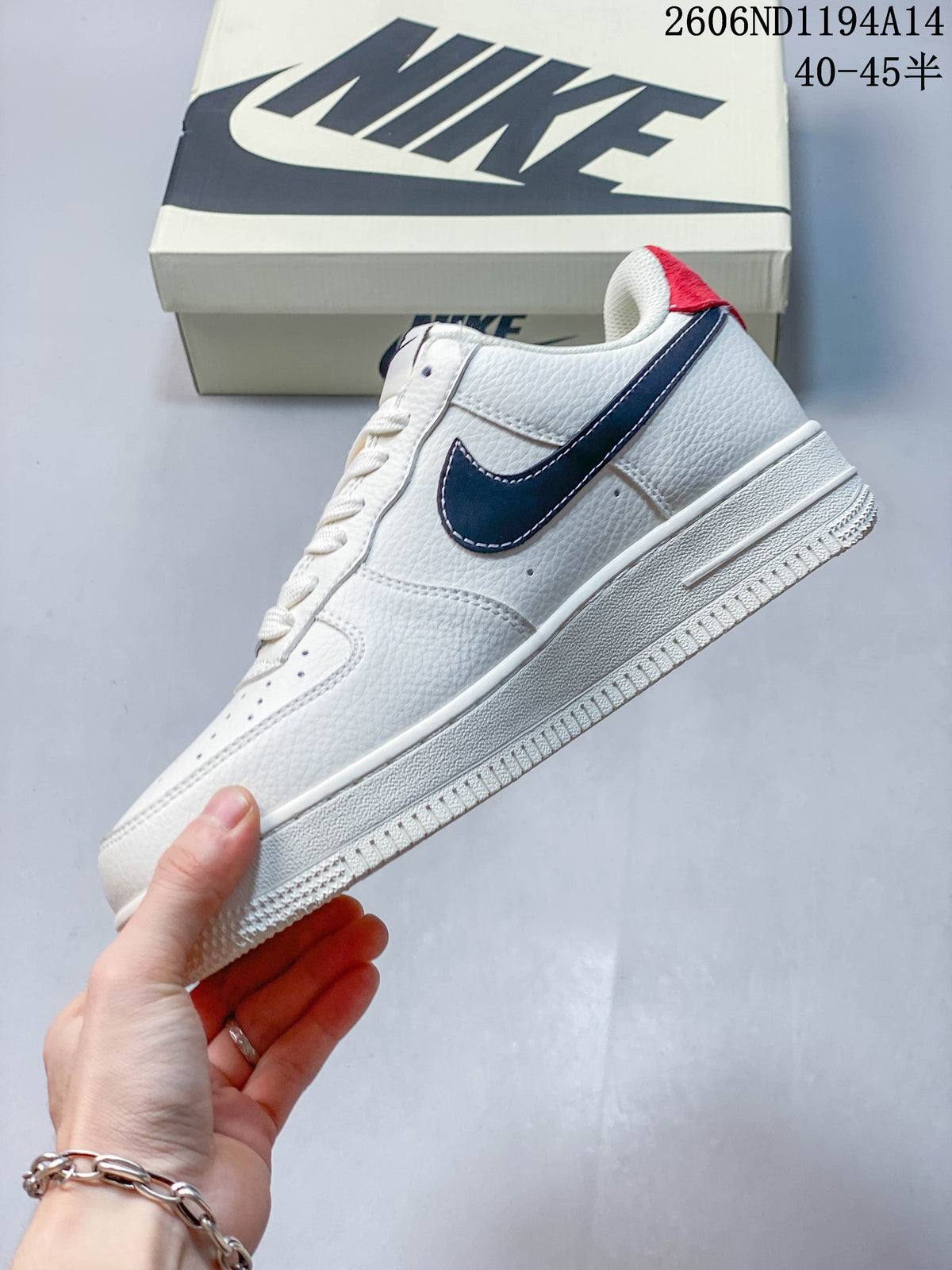Side view of the white low-top sneaker with dark navy Swoosh and red heel accent