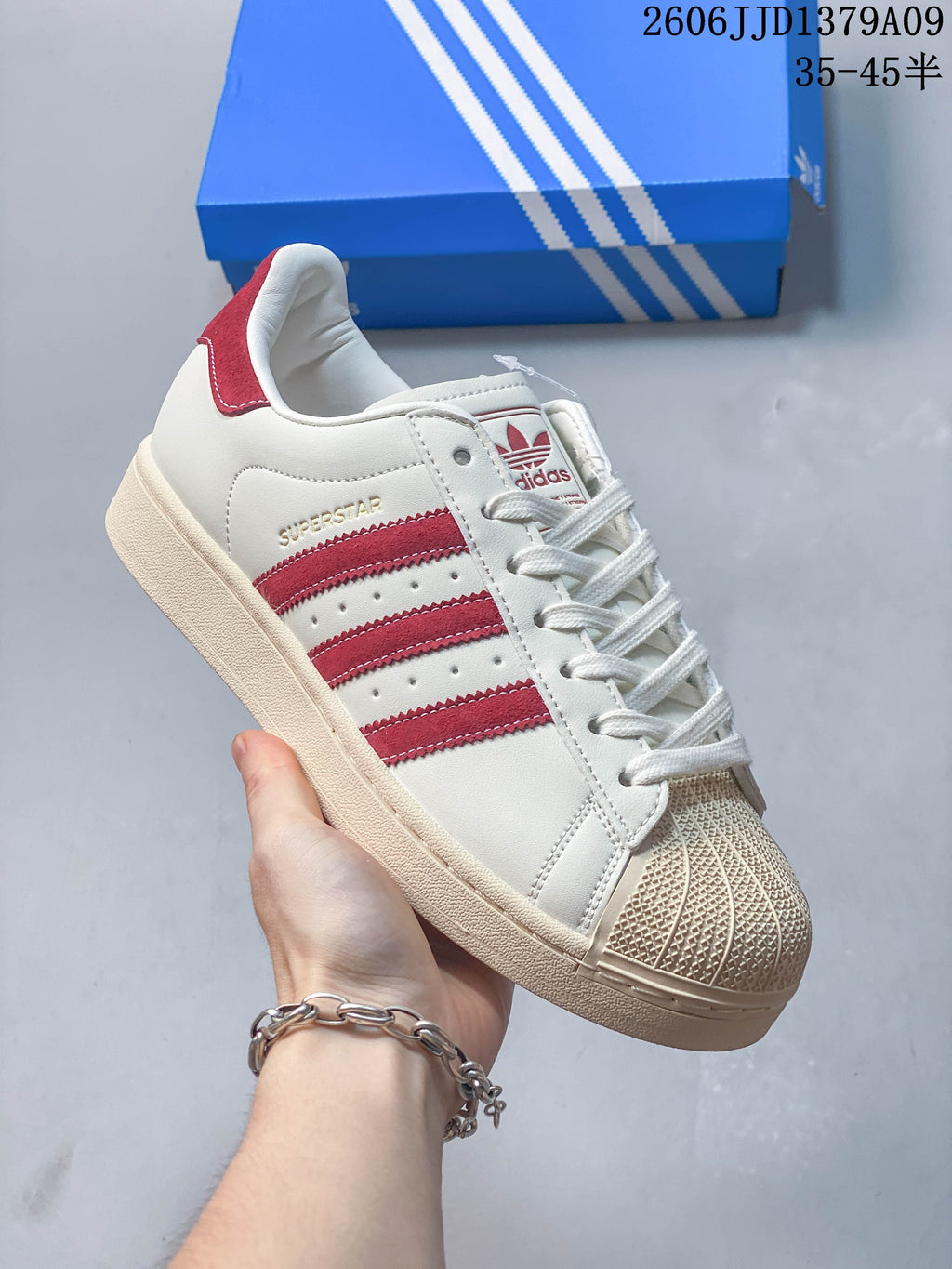Side view of a cream adidas Superstar sneaker with red stripes, a shell toe and a tonal sole.