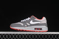 Side view of grey Nike Air Max 1 sneakers with a white Swoosh, crimson accents, and a visible heel Air unit.