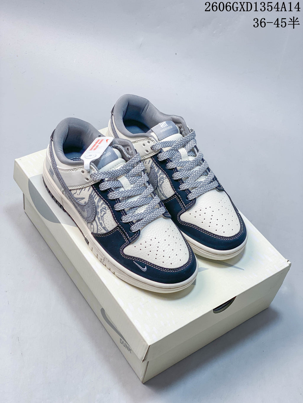 Pair of white, navy, and gray Nike Dunk Low x Undefeated sneakers on a box