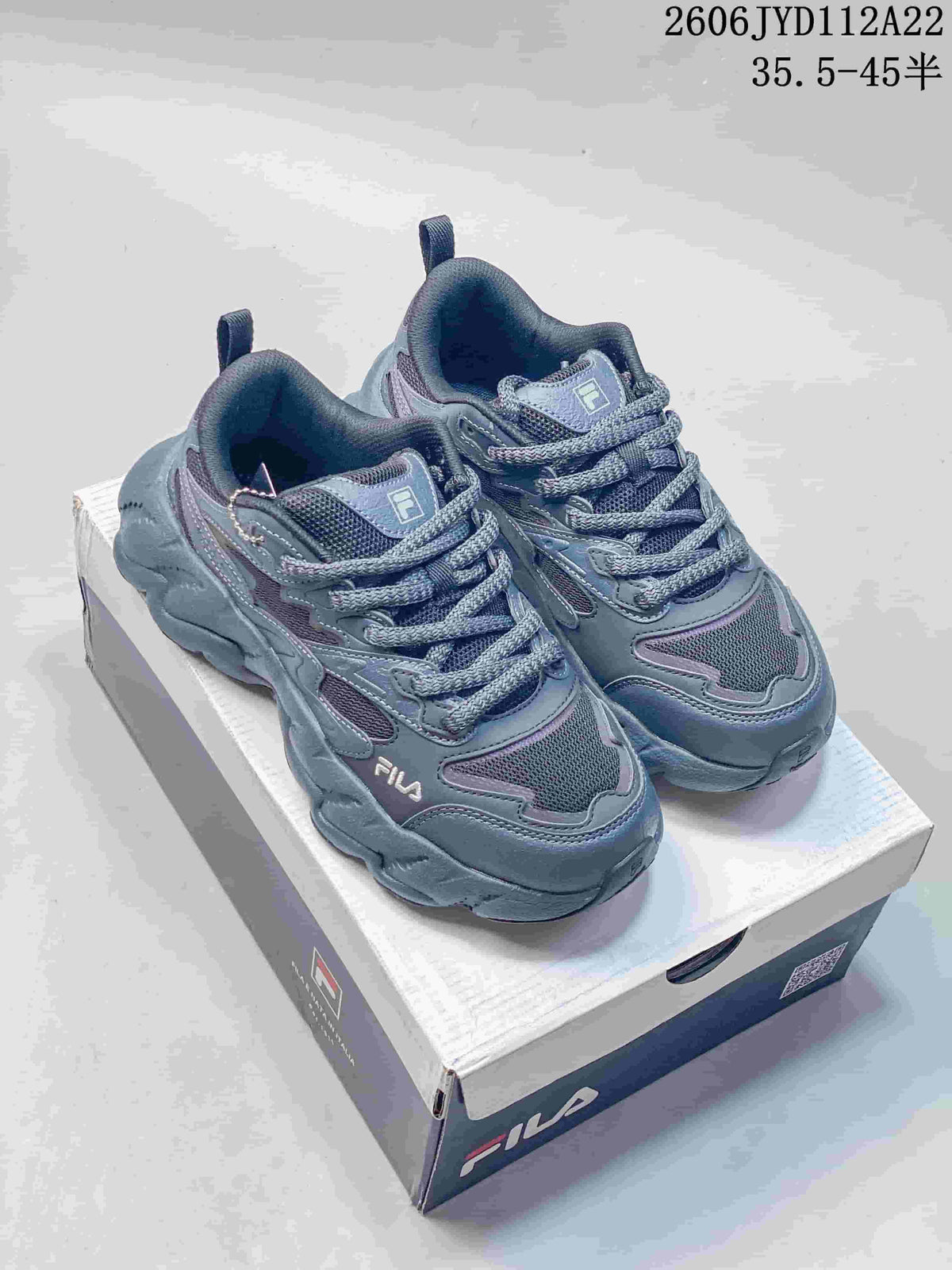 Gray-blue FILA sneakers with a chunky sculpted sole, displayed on a shoebox.