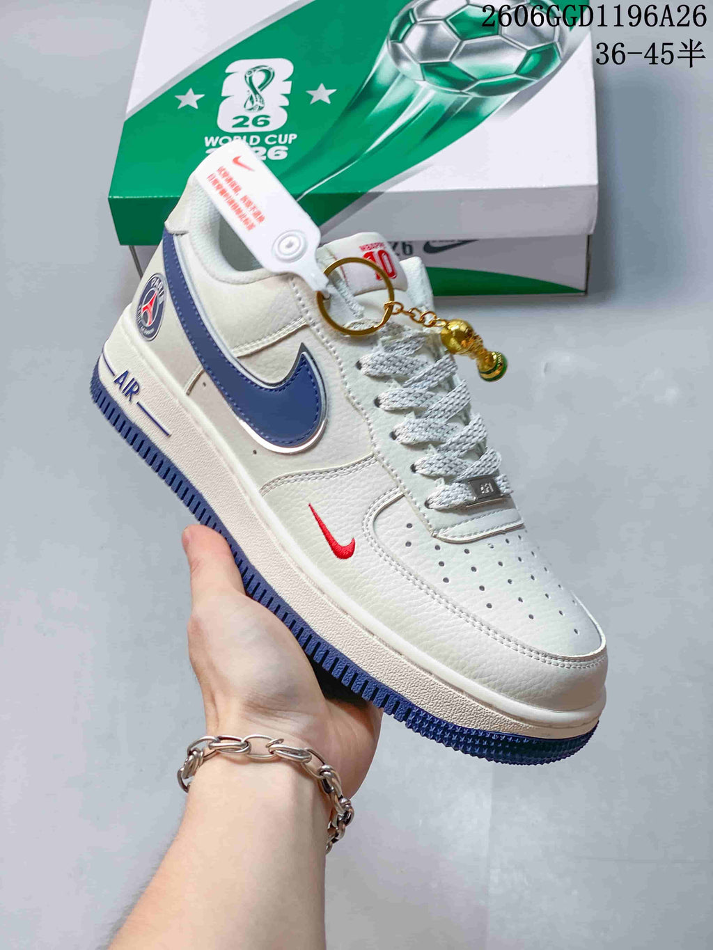 Close-up side view of a white low-top sneaker with a blue Swoosh, red accent Swoosh, blue outsole, and decorative charm.