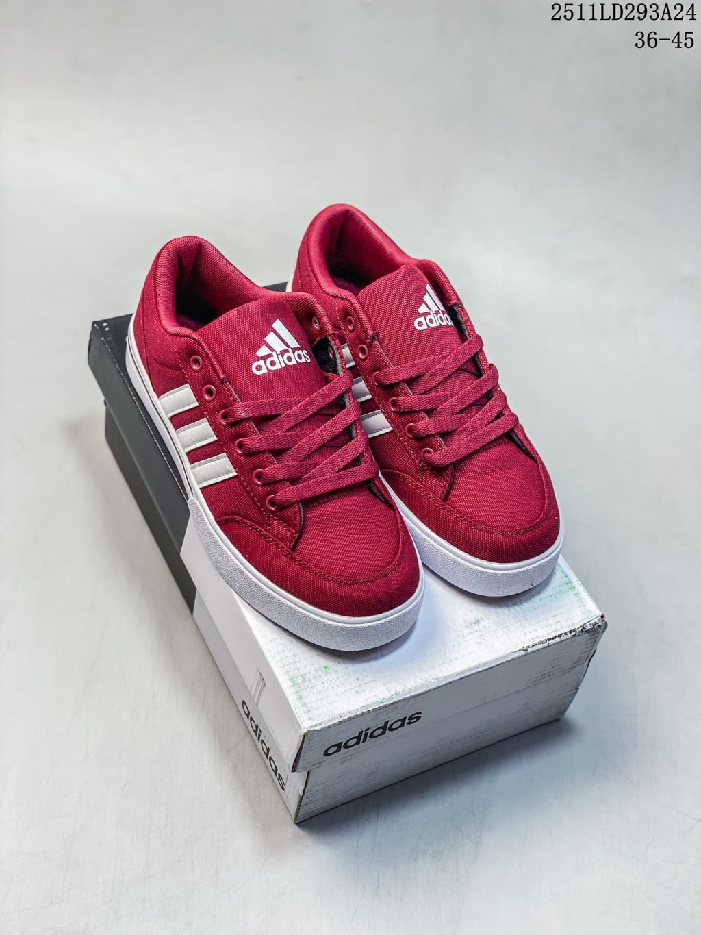 Pair of burgundy Adidas low-top sneakers with white stripes and white soles on a shoebox