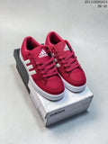 Pair of burgundy Adidas low-top sneakers with white stripes and white soles on a shoebox