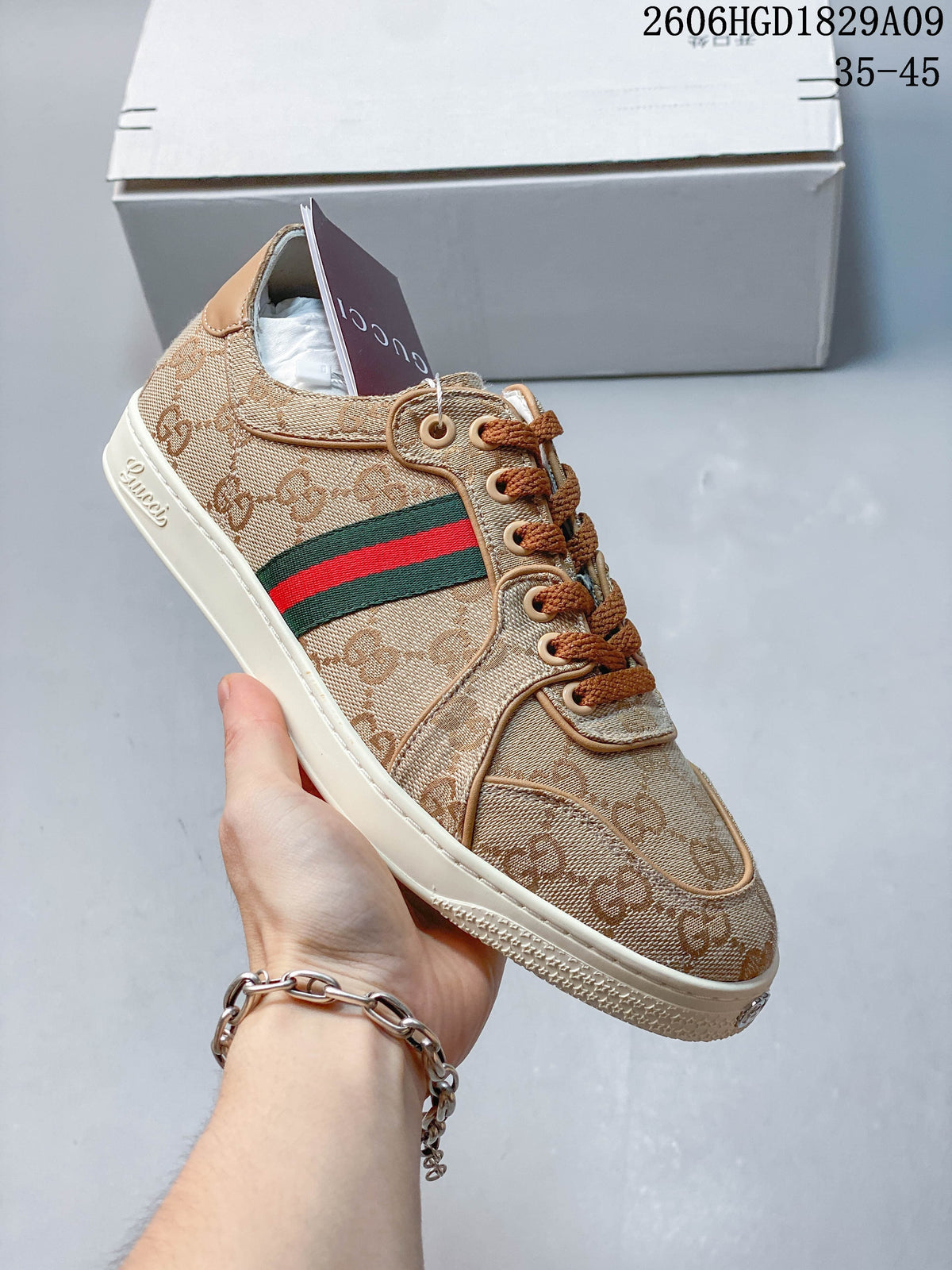 Angled side view of a beige GG-pattern sneaker with brown laces and a green and red stripe