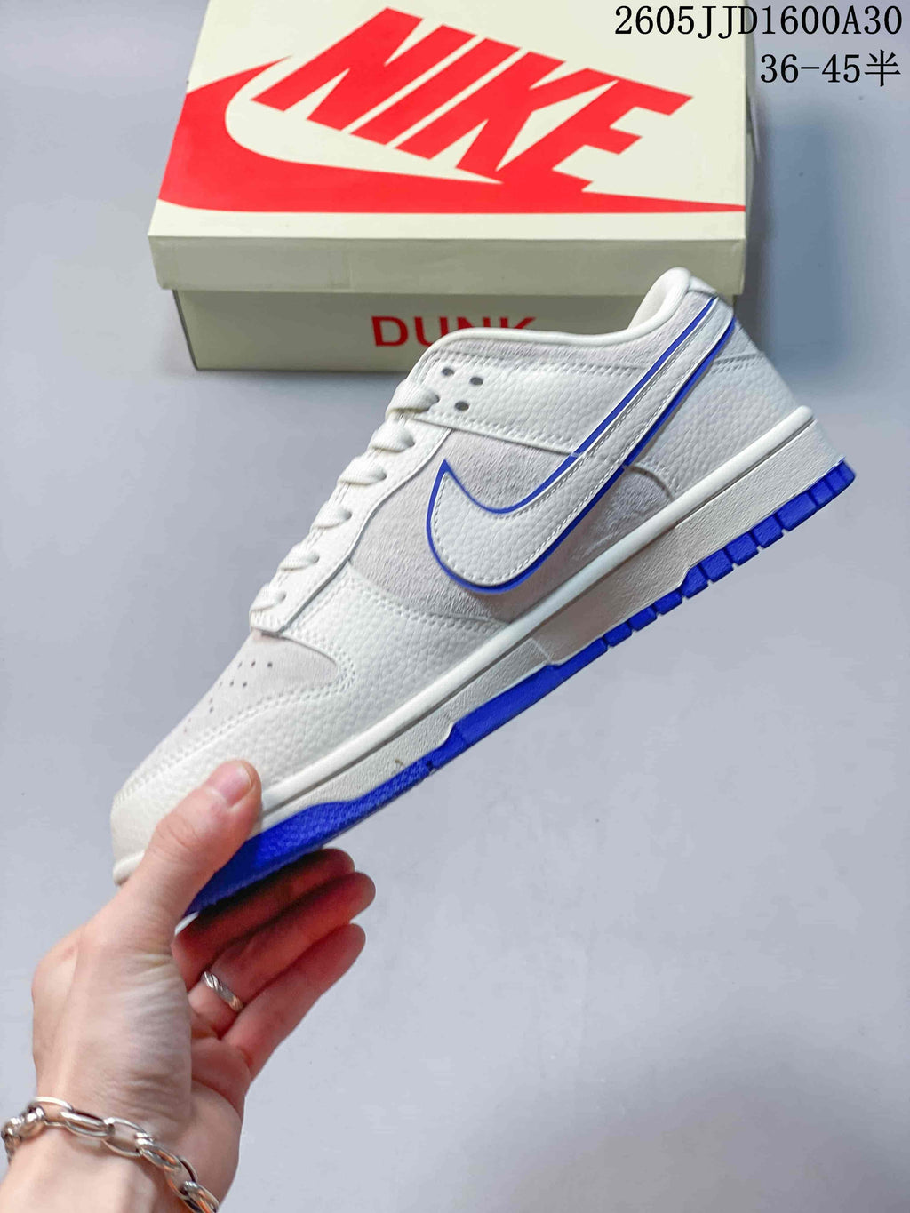 Side view of a white and light gray Nike SB Dunk Low sneaker with blue accents