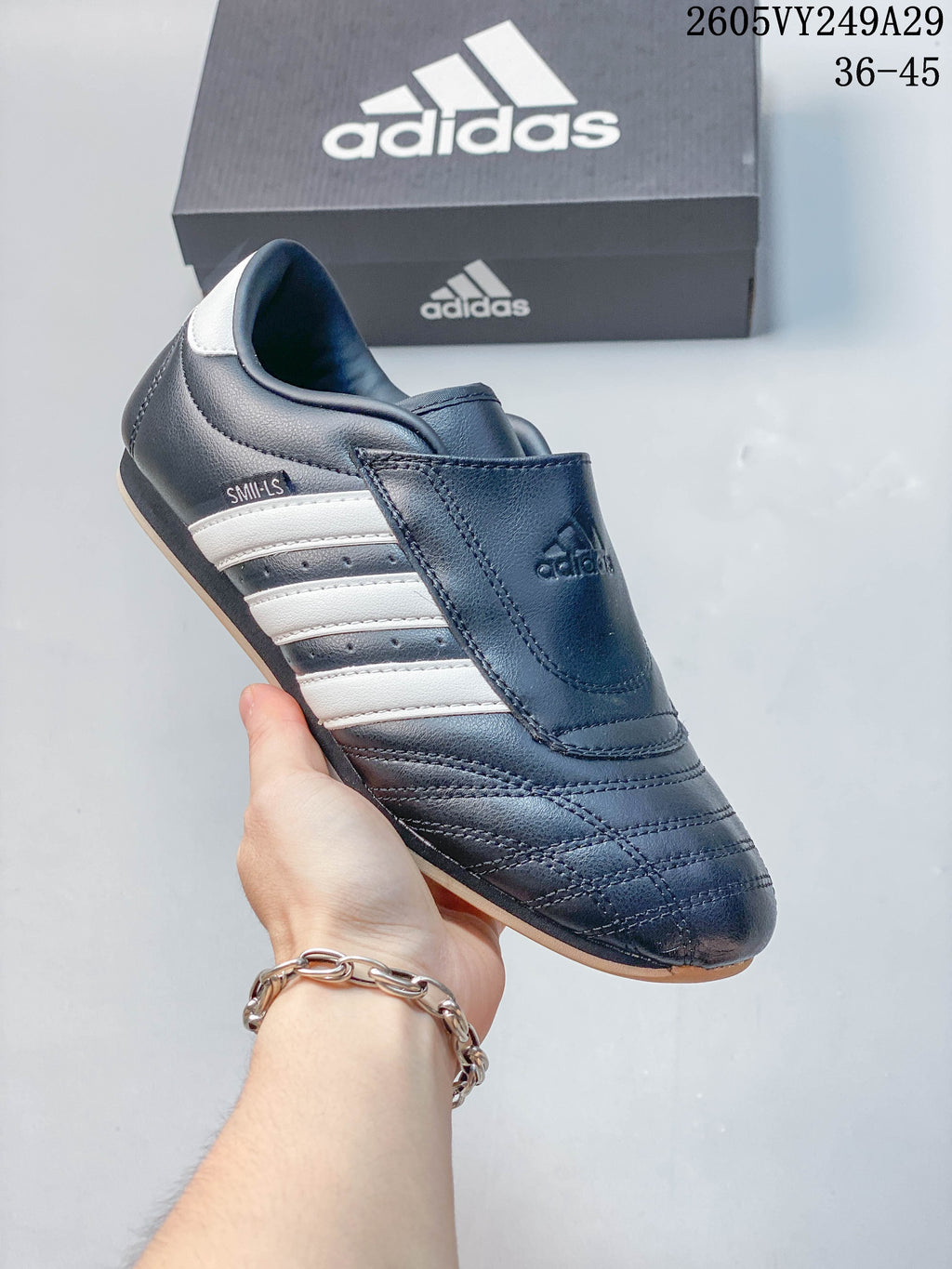 Close-up of a dark low-top shoe with a broad instep strap and white side stripes.
