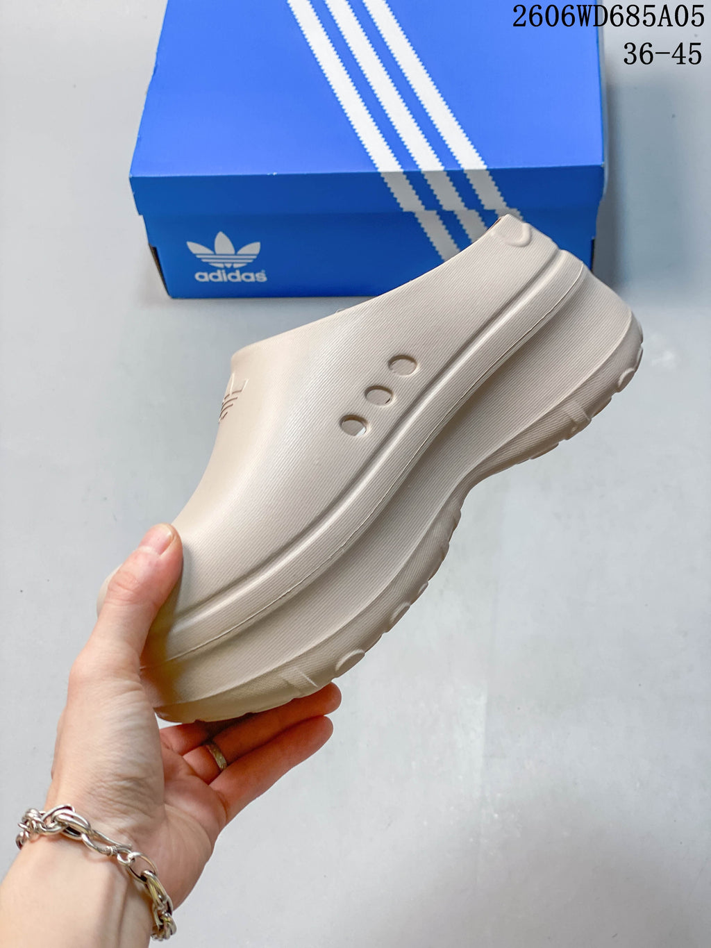 Side view showing the raised sole and ventilation holes of a light beige adidas mule clog.
