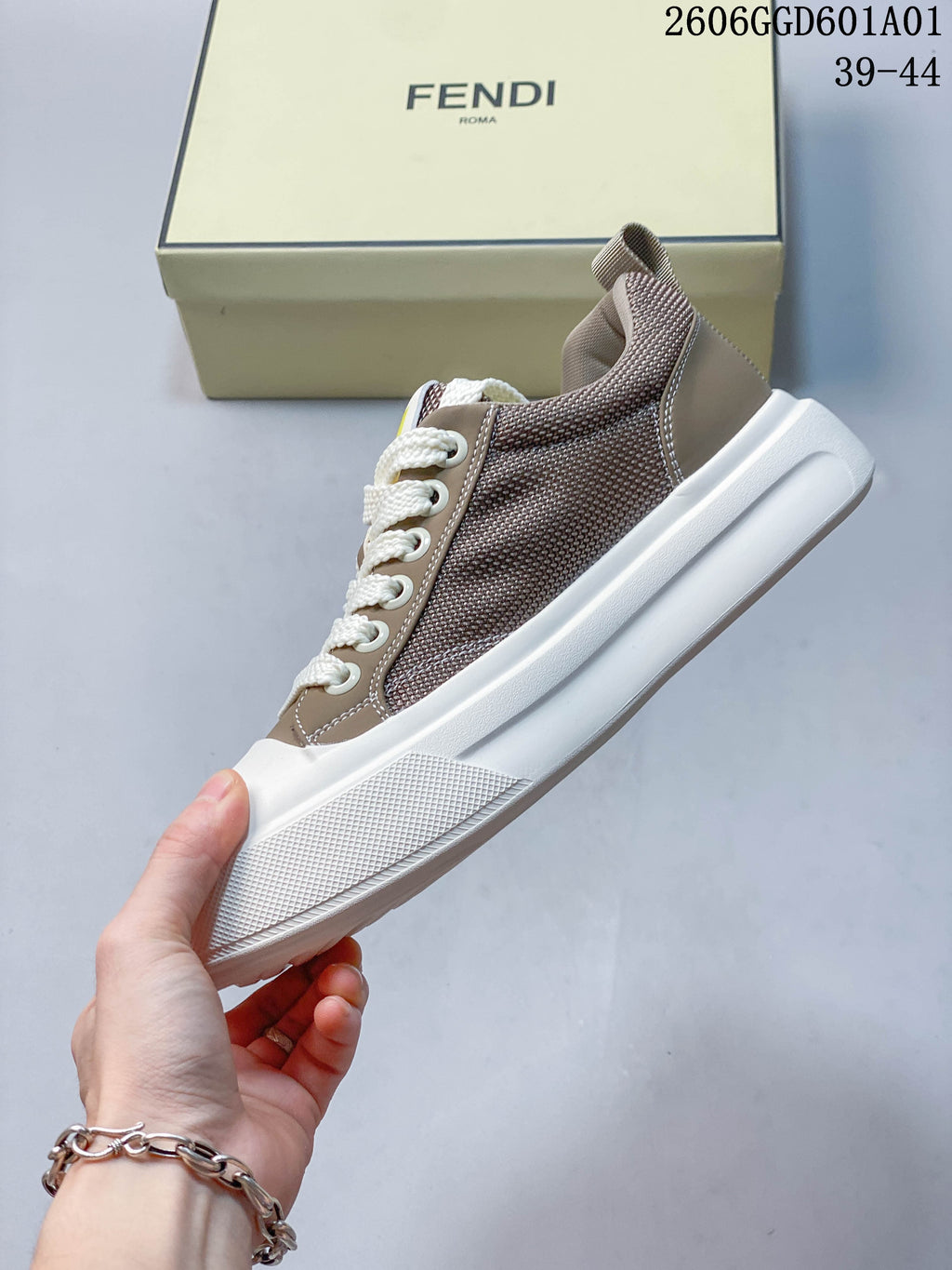 Side view of a taupe and brown low-top sneaker with white laces and sole