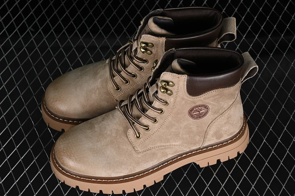 Pair of khaki mid-top lace-up boots showing dark collars and chunky lugged soles.