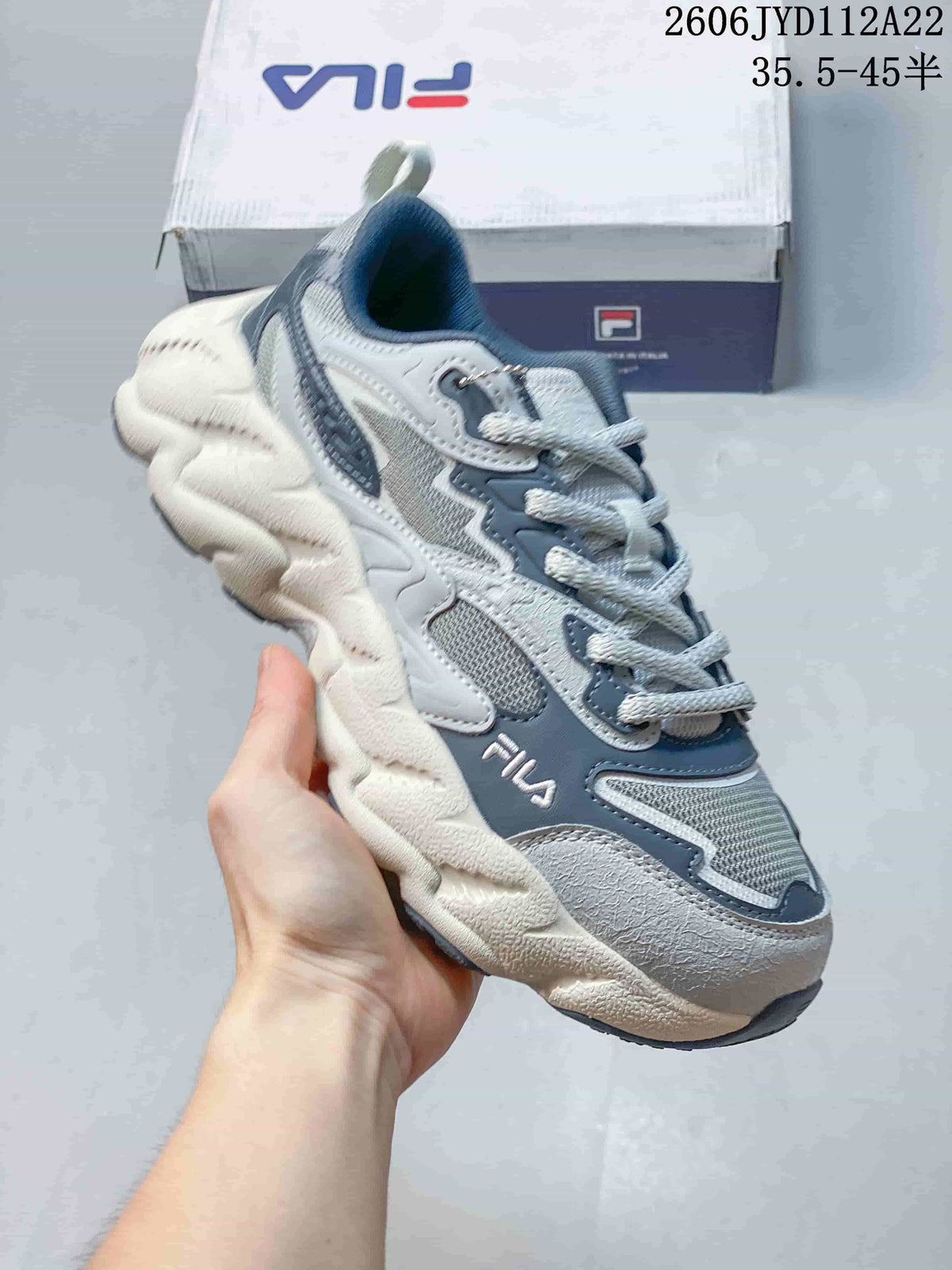 Close view of a light gray FILA sneaker with blue-gray panels and a chunky sole.