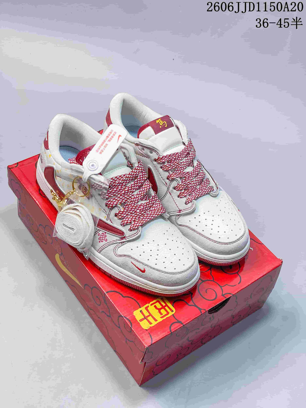 White and burgundy low-top sneakers with patterned laces and decorative accessories on a red box.