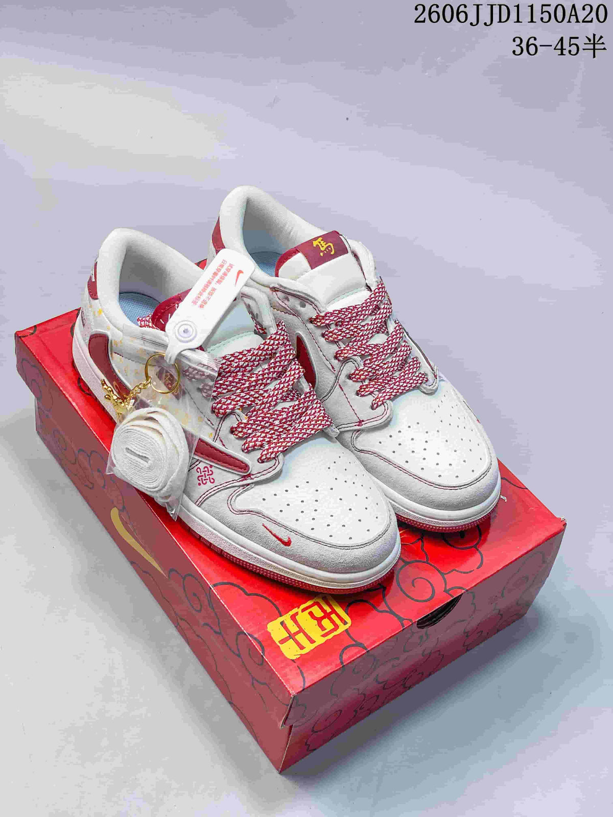 White and burgundy low-top sneakers with patterned laces and decorative accessories on a red box.