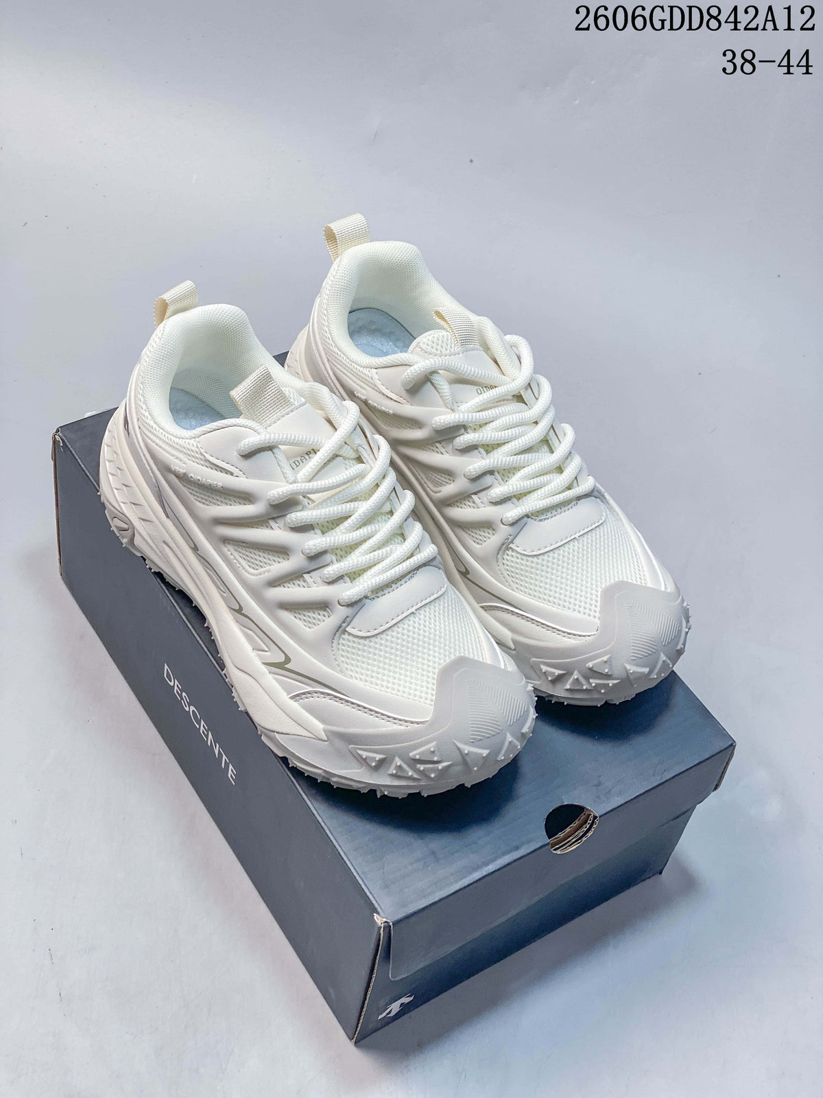 White DESCENTE sneakers shown from above on a branded box; the image displays style code 2606GDD842A12 and the size range 38–44.