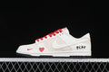 Side view of off-white and beige low-top sneakers with red laces, heart detail, side swoosh, PLAY lettering, and black outsole