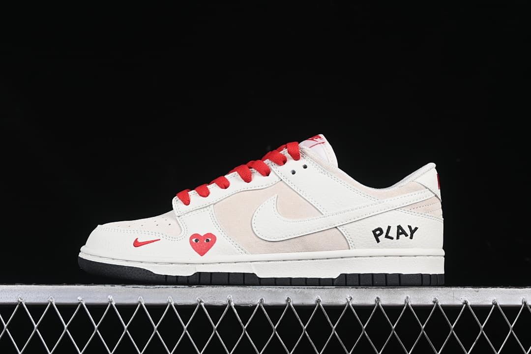 Side view of off-white and beige low-top sneakers with red laces, heart detail, side swoosh, PLAY lettering, and black outsole
