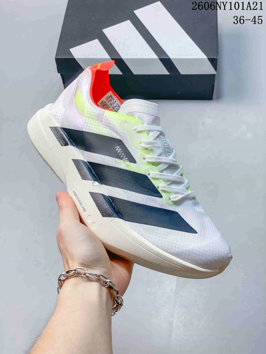 Angled side view of a white Adidas shoe with dark stripes and neon yellow-green and orange-red details.