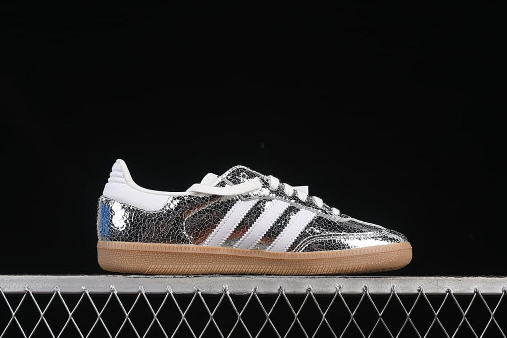 Side profile showing the reflective silver patterned upper, white stripes, and gum-colored sole