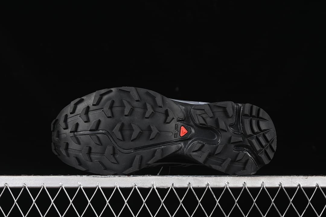 Underside view of the outsole with prominent tread lugs and a red accent.