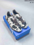 Pair of black-and-white cow-print Adidas Samba OG sneakers with dark laces on a blue box