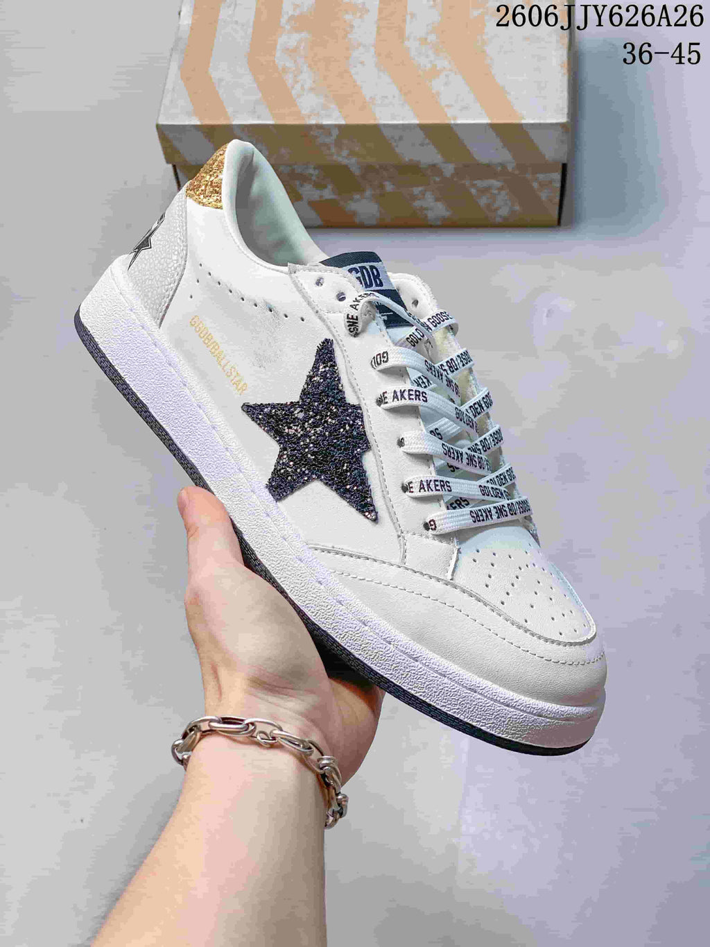 White low-top sneaker with a dark glitter-style star, printed laces, and a distressed-look sole.