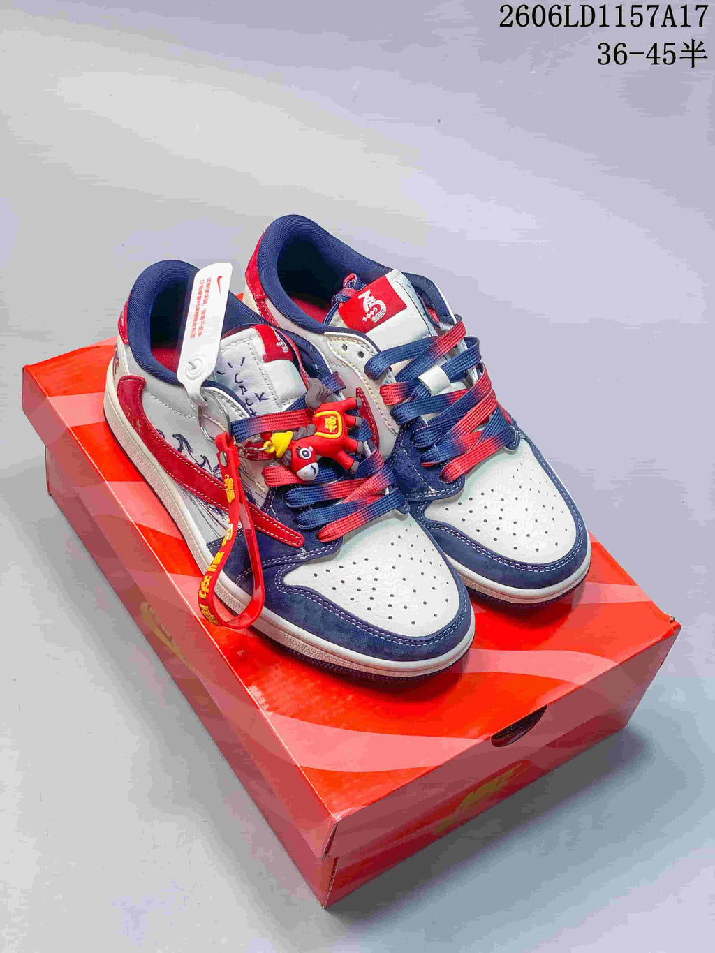Pair of white, navy and red low-top sneakers with lace charms displayed on a red shoe box.
