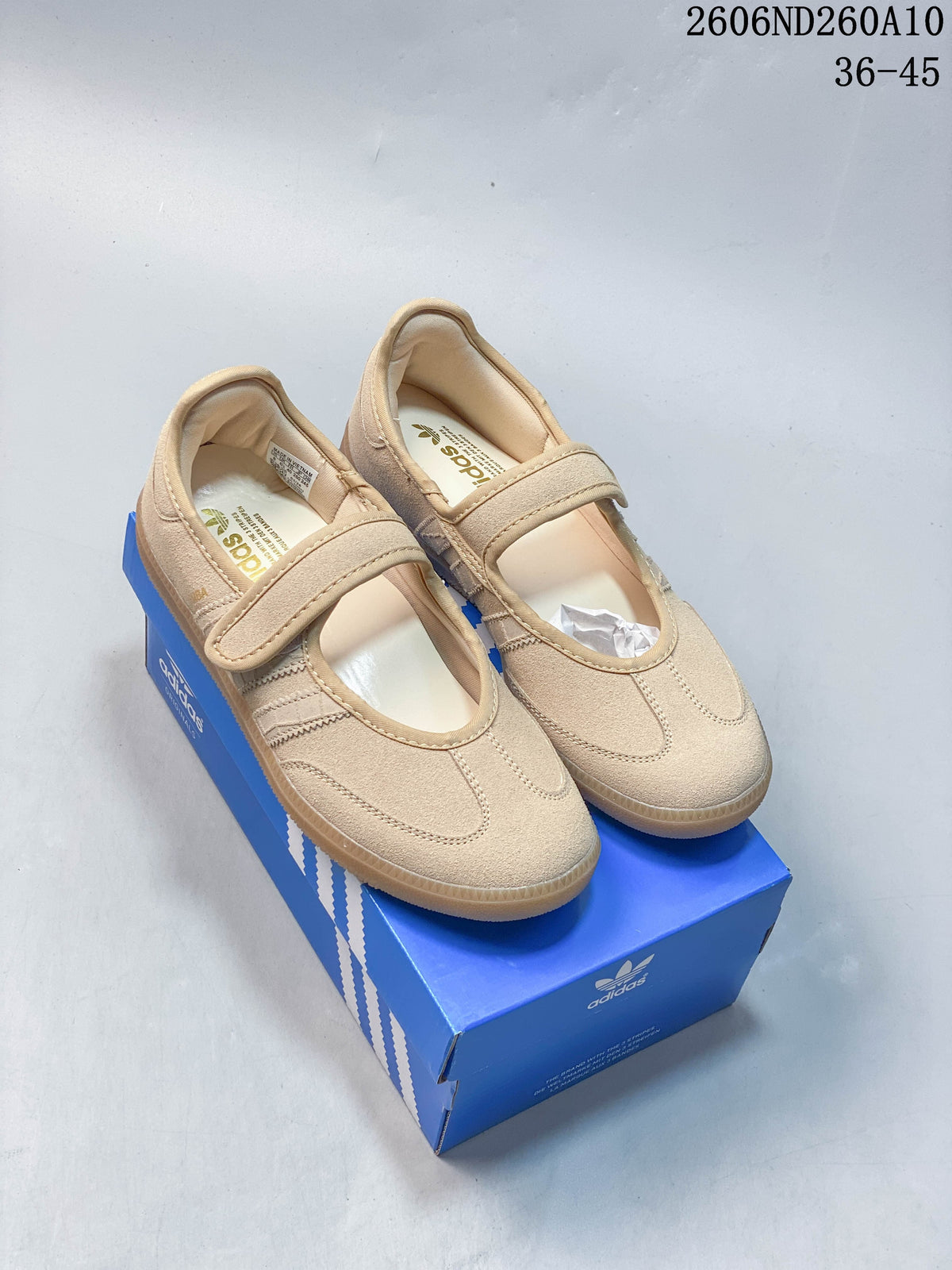 Pair of sand-beige Mary Jane shoes with single straps and gum-colored outsoles on a blue shoe box.