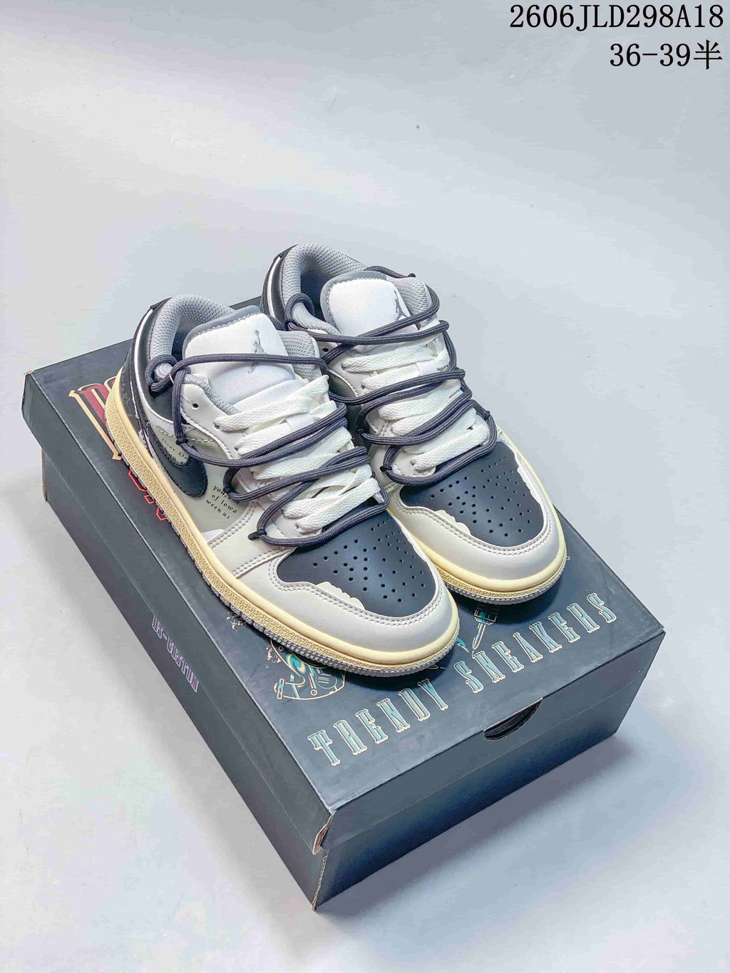 Pair of gray and white Air Jordan 1 Low sneakers with layered strap-style lacing, shown on a graphic shoe box.