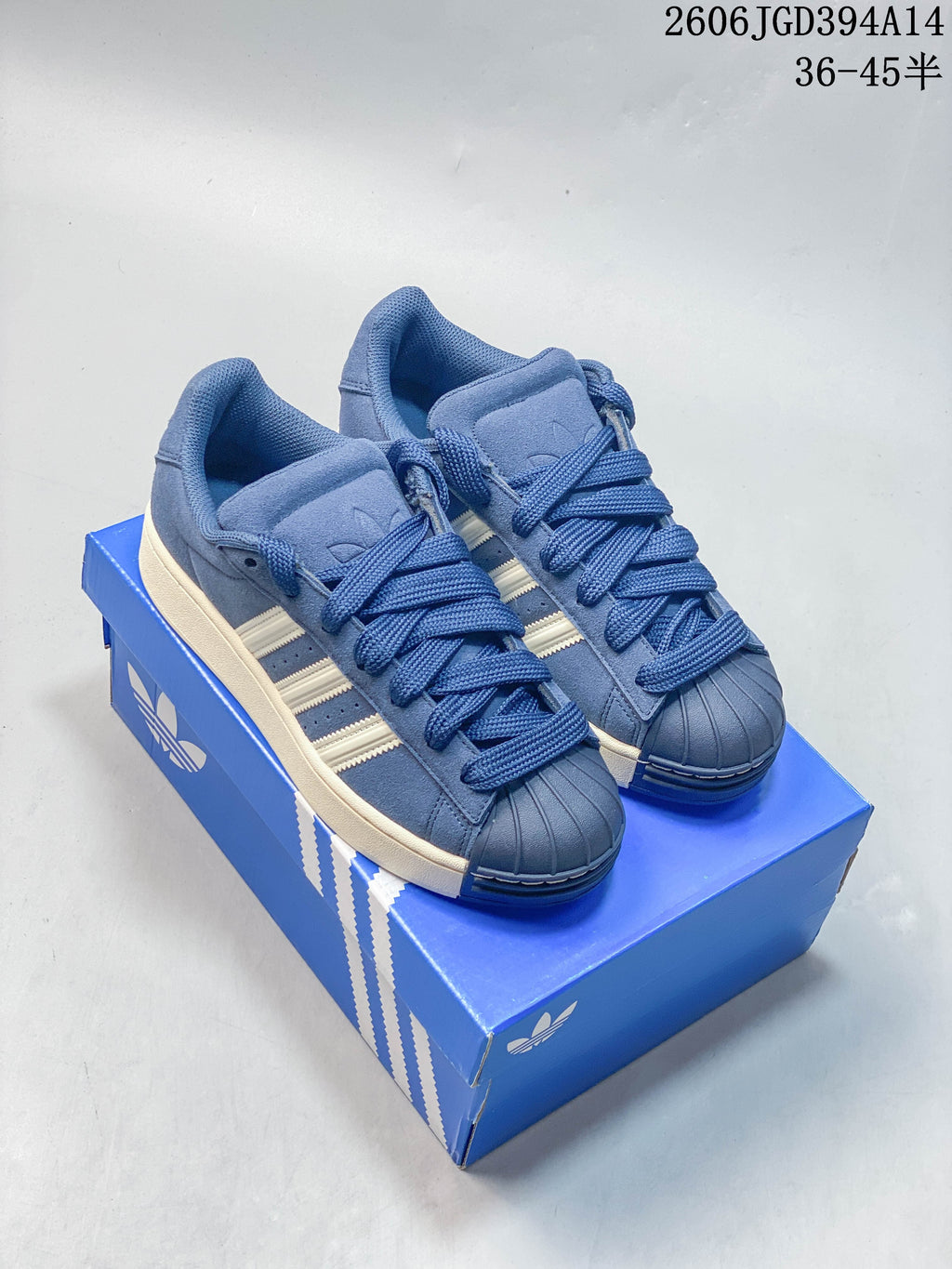 Blue Adidas Originals Superstar-style low-top sneakers with off-white stripes and sole, shown on a blue box