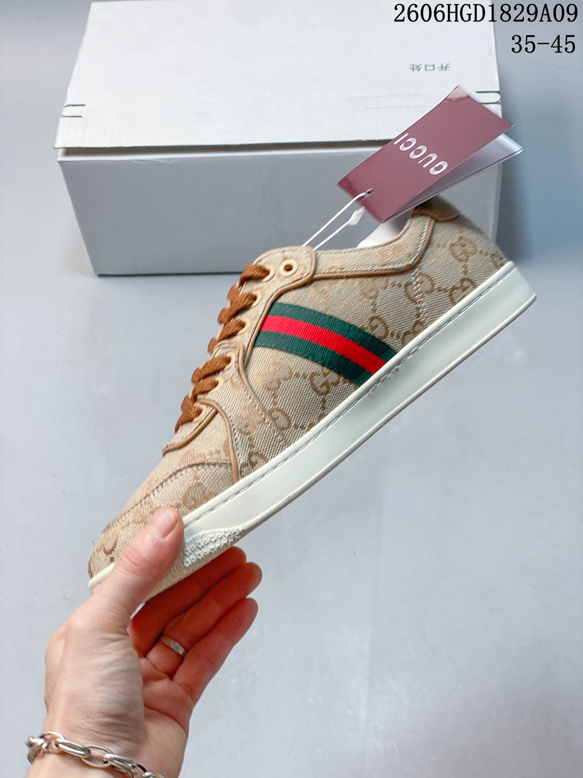 Side view of a beige GG-pattern low-top sneaker with a green and red stripe