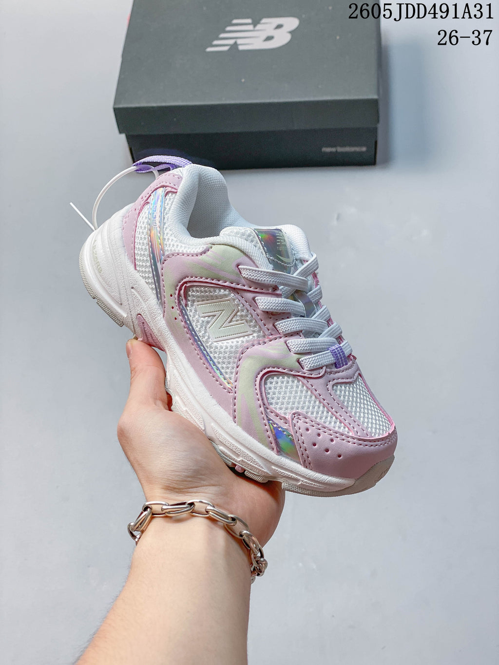 Pink and iridescent-accented kids' New Balance 530 lace-up sneaker shown in hand.