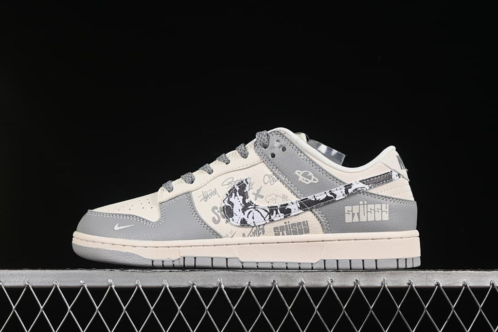 Side view of a light gray and off-white low-top sneaker with patterned graphics and printed lettering.