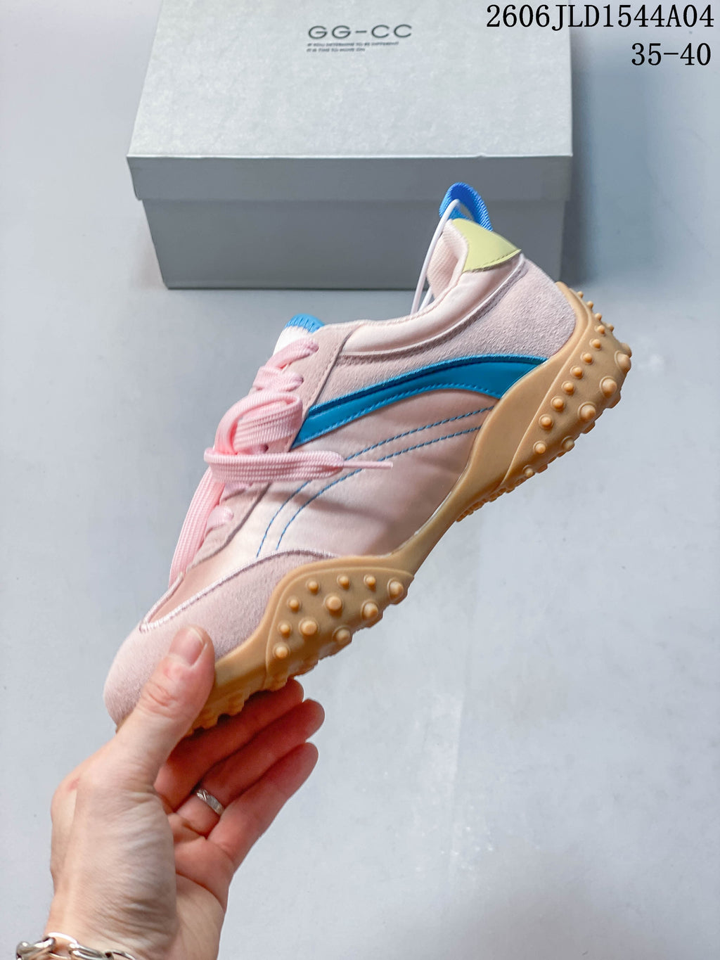 Side profile of a pale pink sneaker with a blue stripe, pink laces, and tan nubbed outsole.
