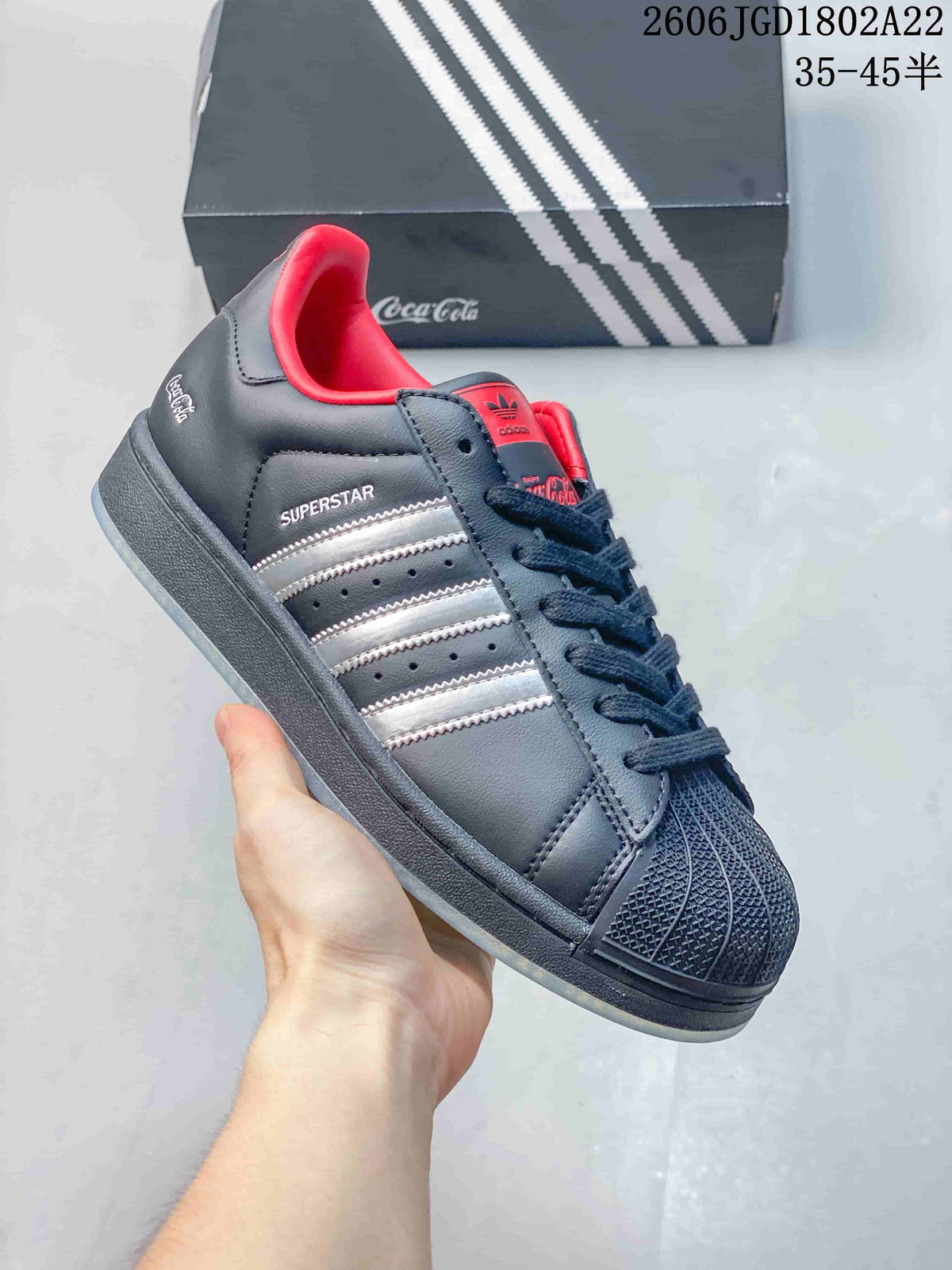 Angled side view showing silver stripes, Superstar lettering, Coca-Cola details, and the textured toe.