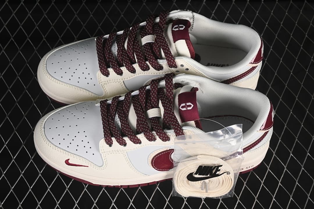 Top view of a pair of cream and white low-top sneakers with burgundy laces and an additional set of light-colored laces