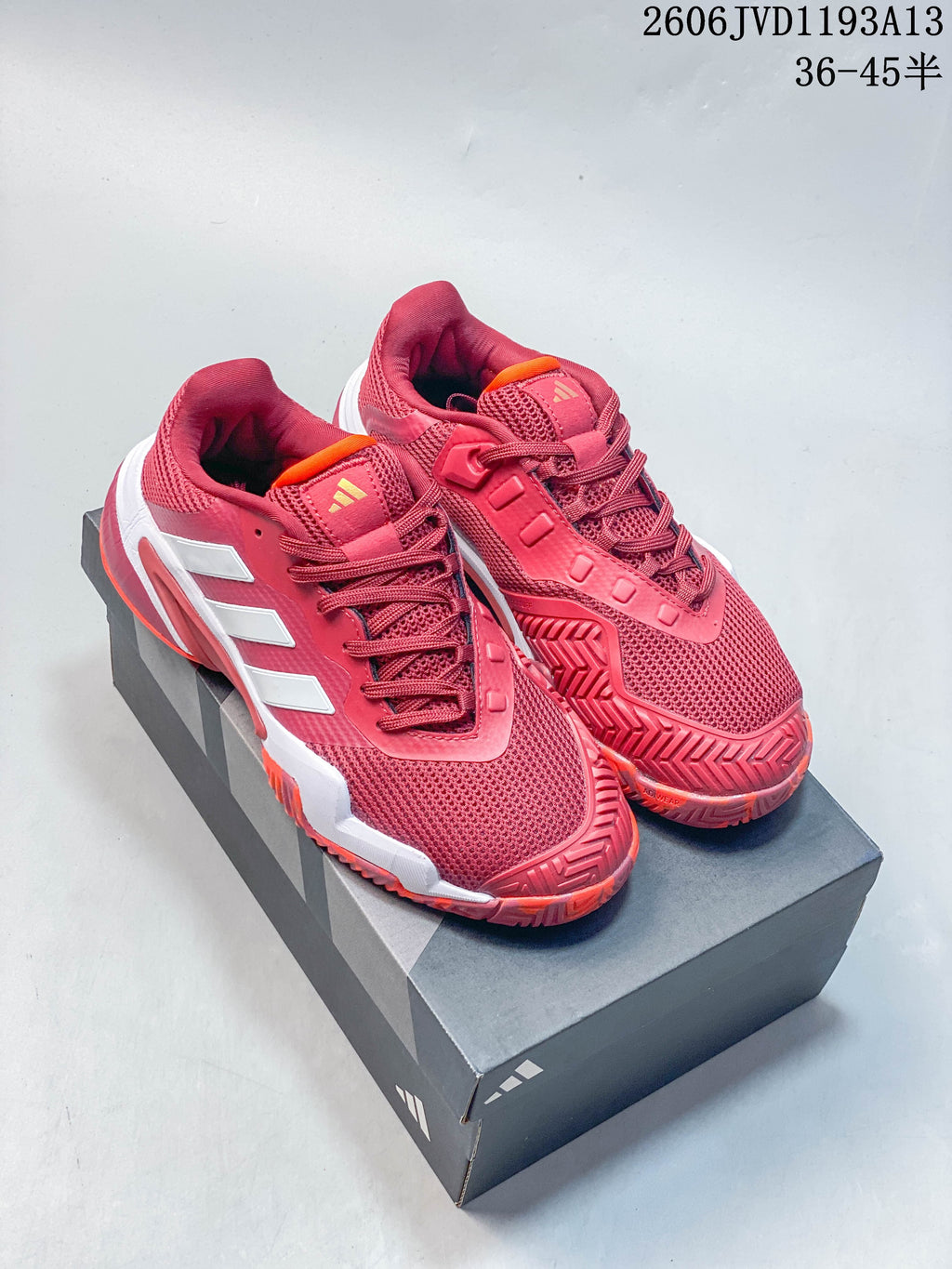 Pair of red Adidas Barricade 13 tennis shoes with white stripes and orange accents, shown on a shoe box.