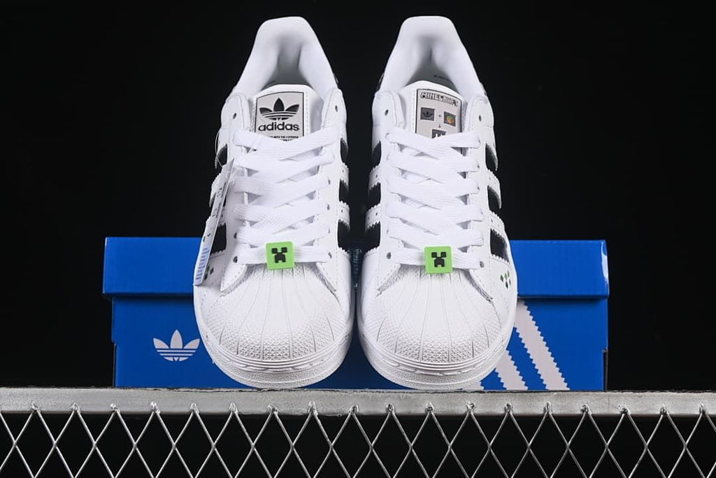 Front view of the pair showing shell toes, white laces, and green lace accessories