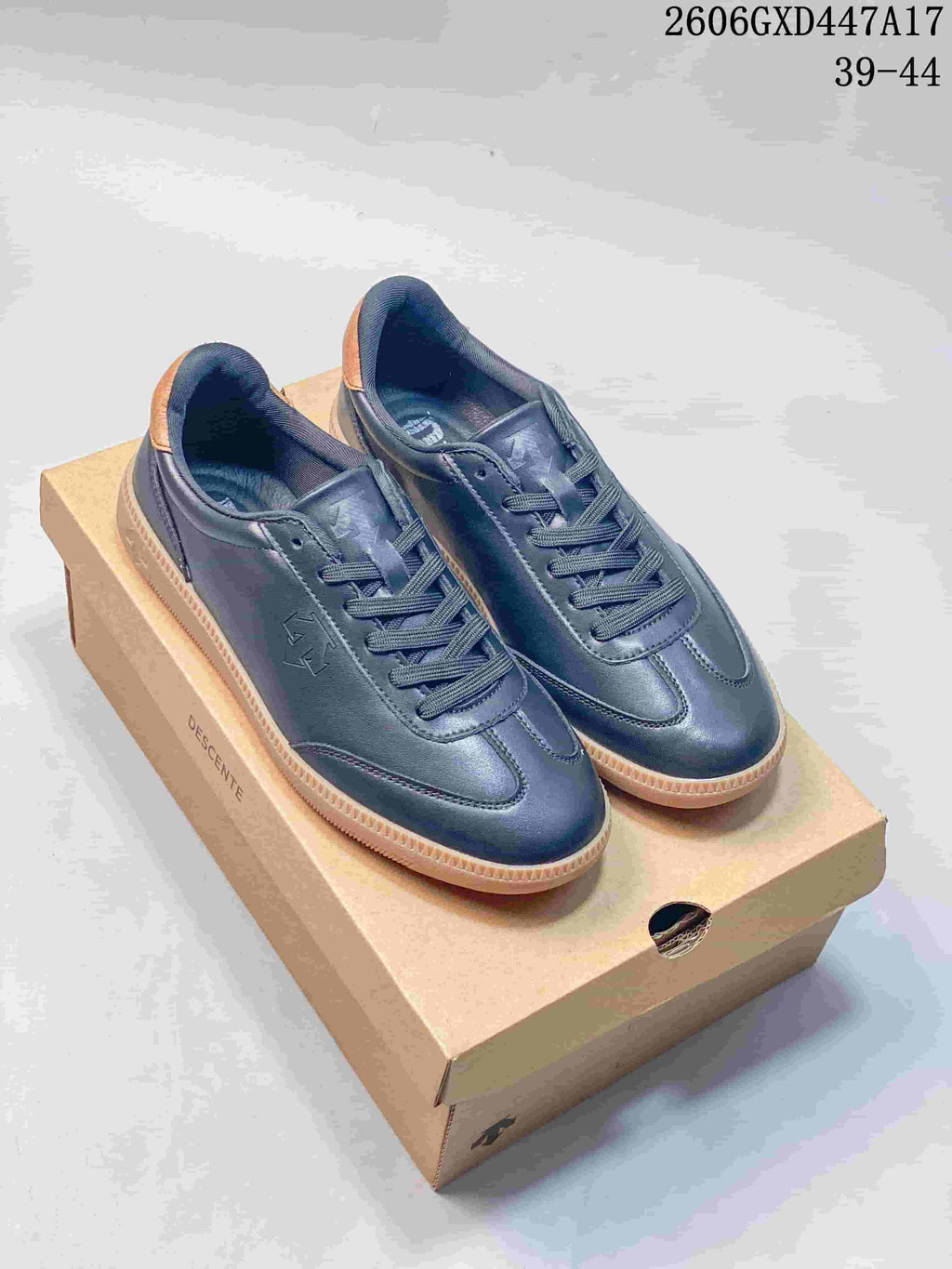 Pair of navy DESCENTE Chron Chron sneakers with tan heel details and gum soles on a branded box.
