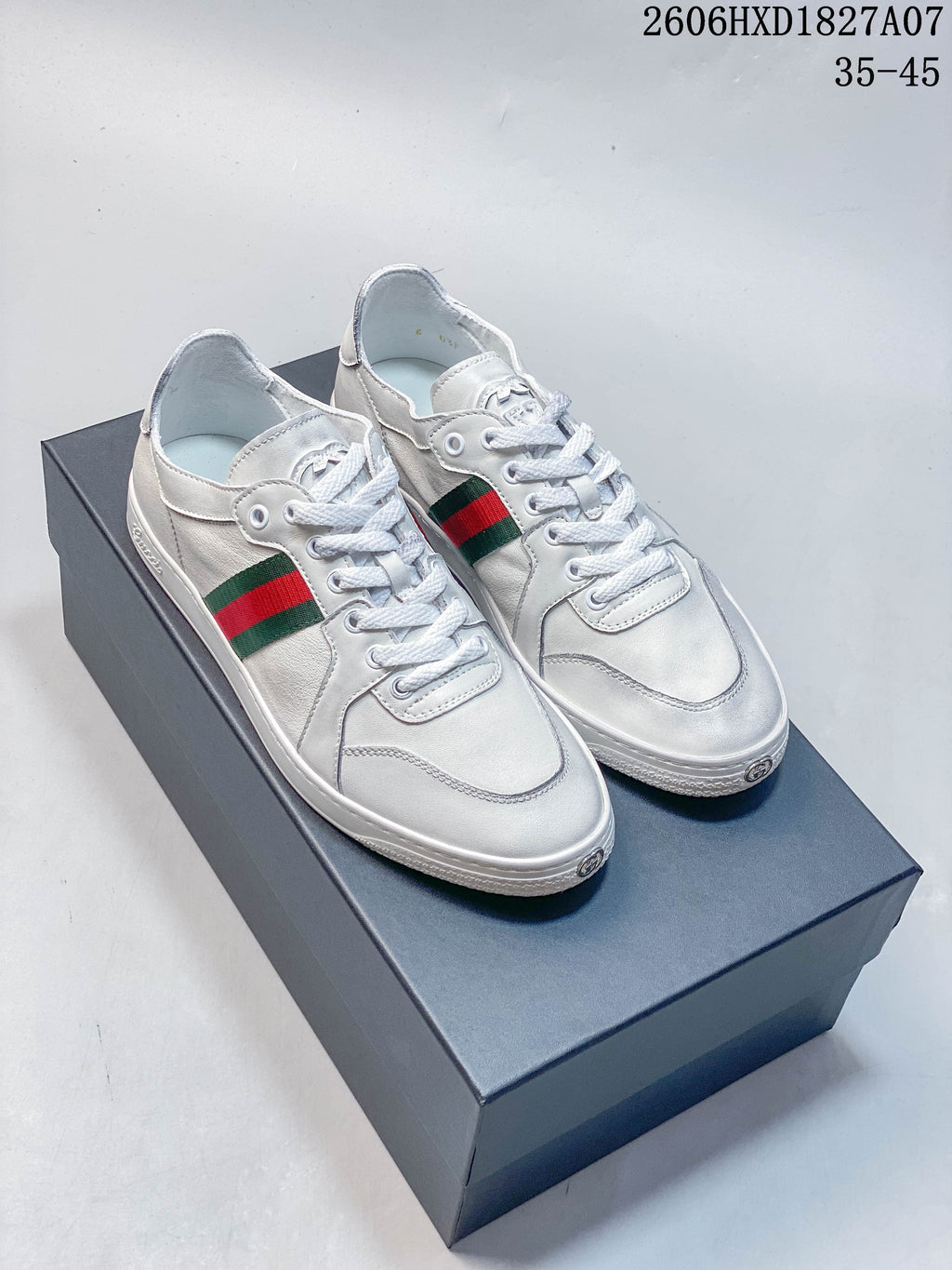 Pair of white low-top sneakers with green-and-red side stripes, shown on a box.