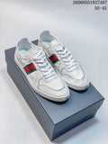 Pair of white low-top sneakers with green-and-red side stripes, shown on a box.