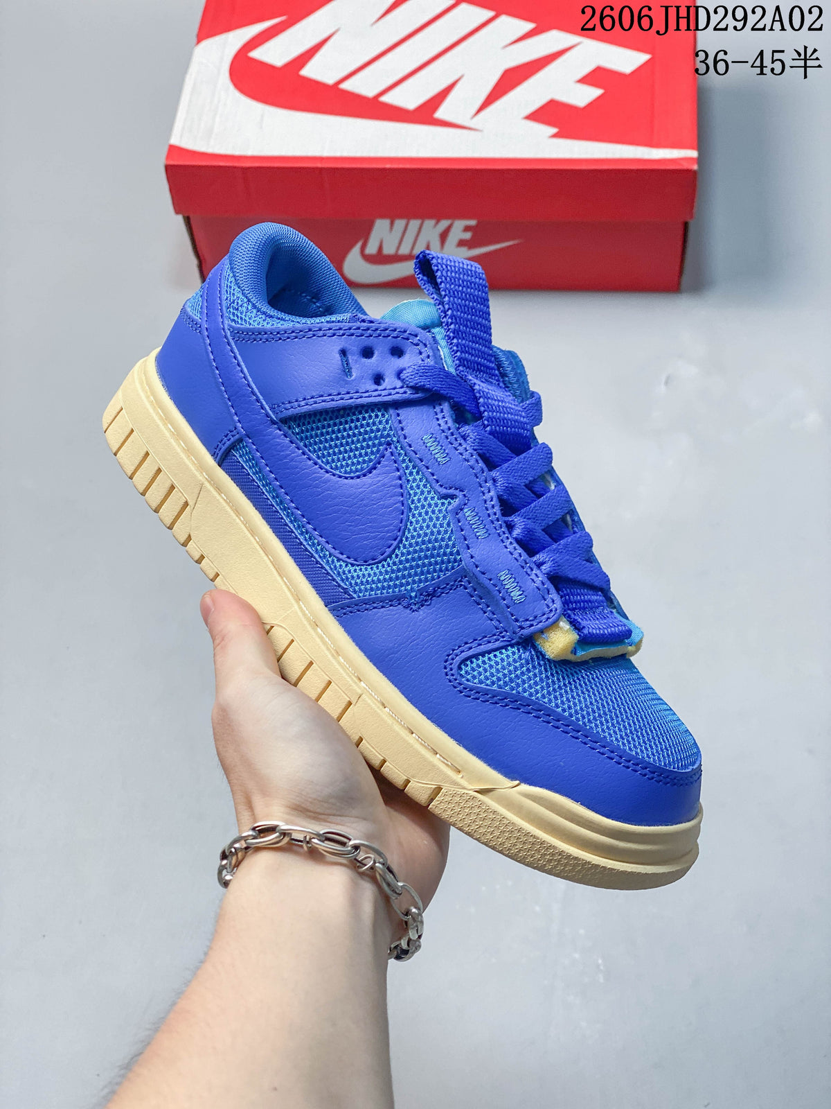 Blue Nike SB Dunk low-top sneaker with a pale contrasting sole, shown beside a Nike shoe box.