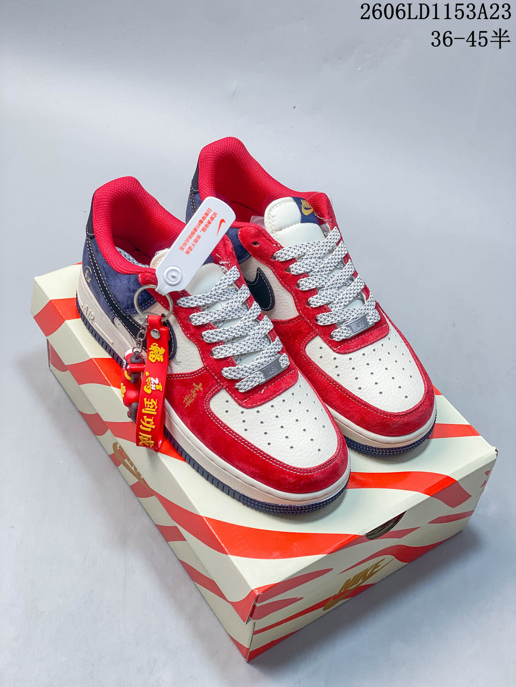 Red, white, and navy low-top sneakers with patterned laces and a hanging charm on a decorative box