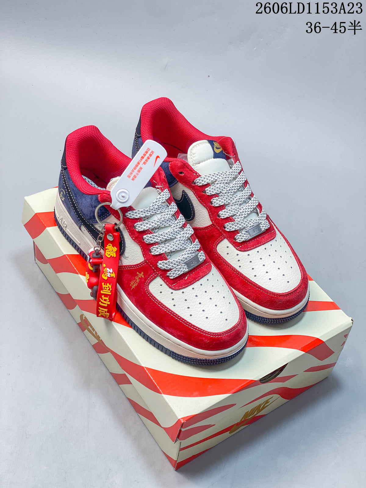Red, white, and navy low-top sneakers with patterned laces and a hanging charm on a decorative box